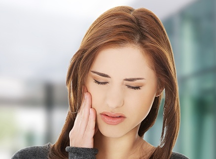 Woman in need of restorative dentistry holding cheek