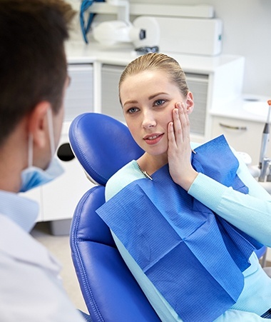 Woman in dental chair holding cheek before restorative dentistry treatment
