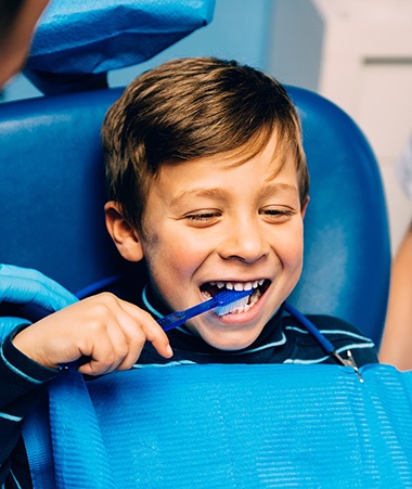 Child smiling while brushing their teeth in treatment chair