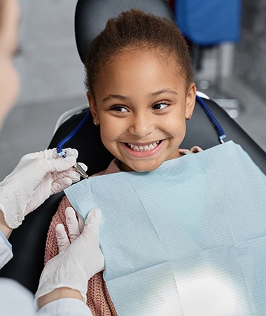Dentist placing bib on smiling child in treatment chair