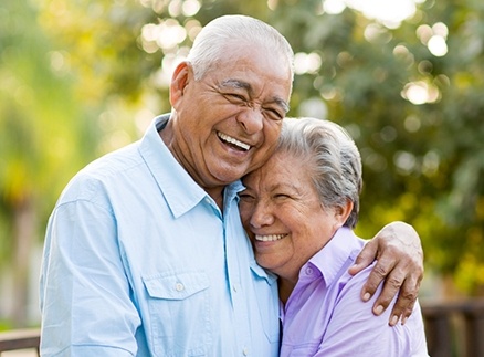 Older man and woman laughing together outdoors after dental implant tooth replacement