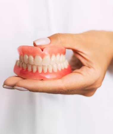 dentist holding a set of full dentures in their hand 