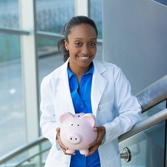 smiling dentist holding a pink piggy bank 