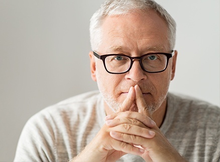 Older man with glasses covering damaged smile before emergency dentistry