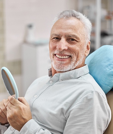 An older man holding a mirror and showing off his new smile in Springfield