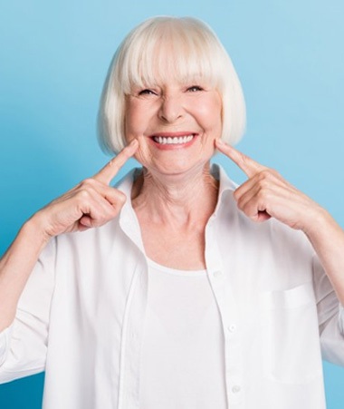 a woman smiling and pointing at her dental implants