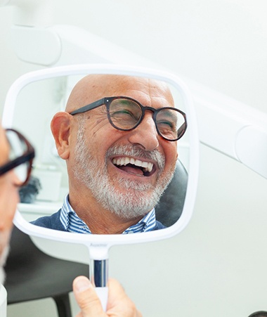 A man smiling in the mirror at his new dental implants