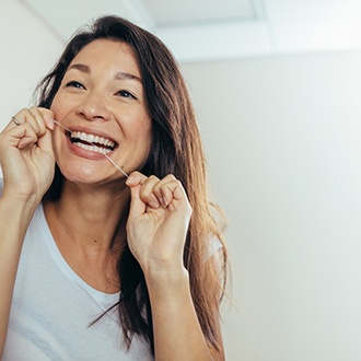 Woman smiling while flossing in bathroom
