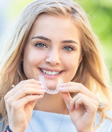 Woman holding clear aligner from Invisalign in Springfield