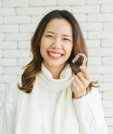 woman in white sweater holding aligner in front of white brick wall 