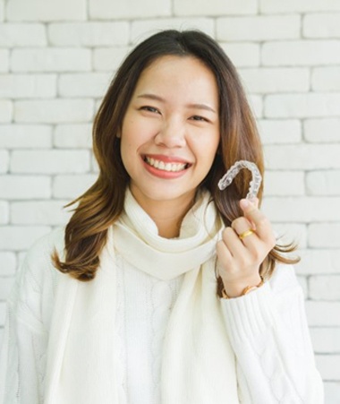 woman in white sweater holding aligner in front of white brick wall