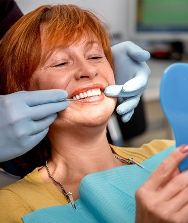 Older woman in dental chair looking at her smile after dental bridge placement