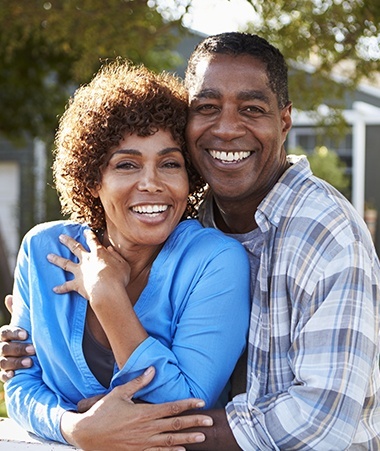 Man and woman smiling together outdoors after receiving dentures