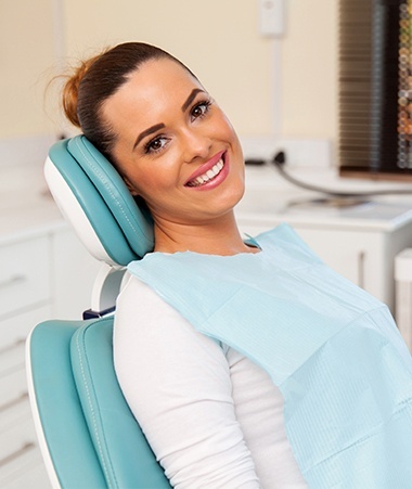 Woman in dental chair smiling after dental implant tooth replacement