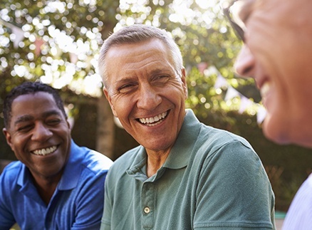 Three older men with healthy smiles after gum disease treatment laughing outdoors