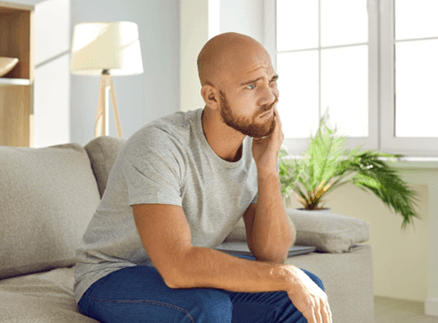 Man sitting on couch with discomfort from failed dental implant in Springfield, NJ
