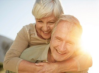 Older man and woman smiling outdoors after replacing missing teeth