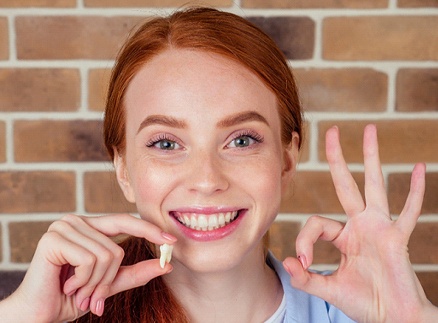 Woman holding tooth and smiling after tooth extraction in Springfield