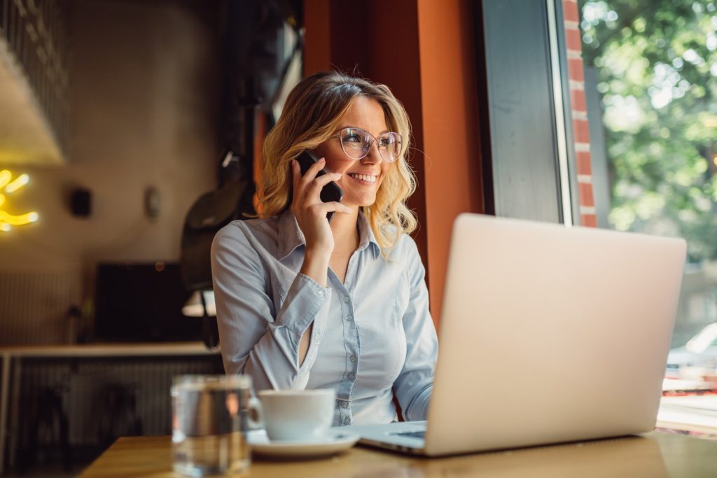 Woman with glasses smiling while talking on the phone and working