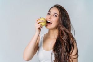Smiling woman holding apple next to her mouth