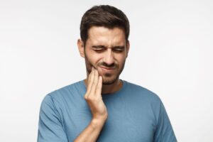 Man in blue shirt touching his hand to his jaw in pain.