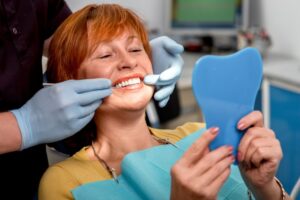 Woman admiring dental implants in the dentist's chair, holding a mirror. 
