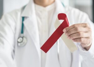 Dentist holding red ribbon for oral cancer awareness.